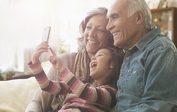 Grandparents and granddaughter taking selfie on sofa